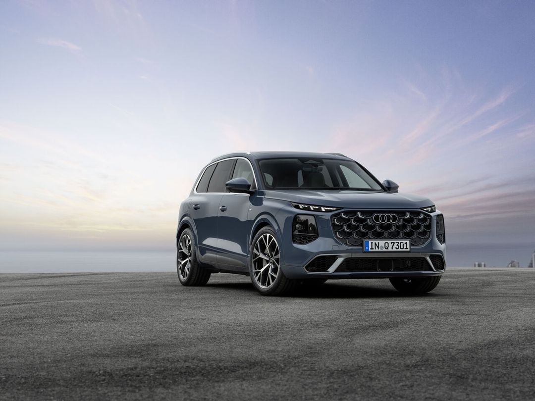Audi Q7 III generacji — ujęcie 3/4 z przodu, kolor stalowy błękit, niemieckie tablice rejestracyjne, dramatyczne niebo w tle