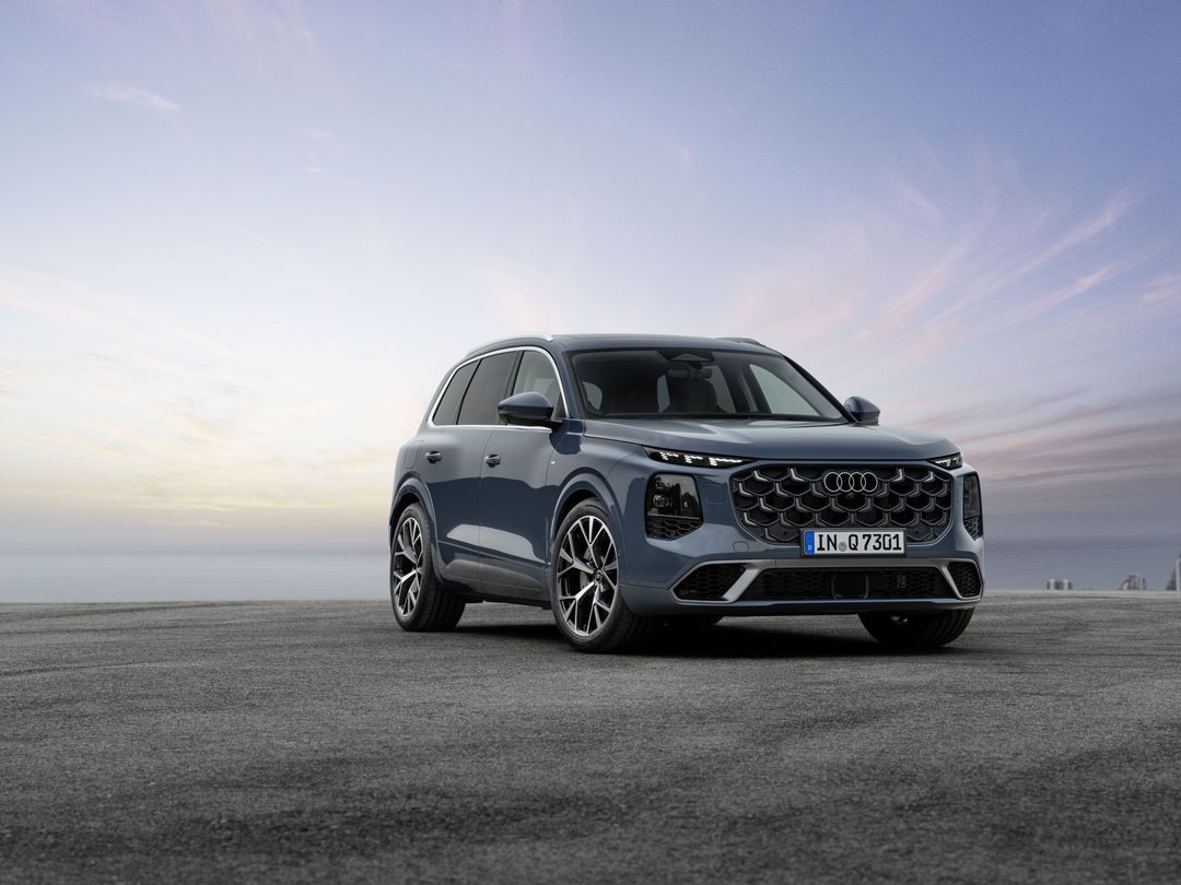 Audi Q7 III generacji — ujęcie 3/4 z przodu, bliźniacza kompozycja, kolor stalowy błękit, horyzont z delikatnym zachmurzeniem