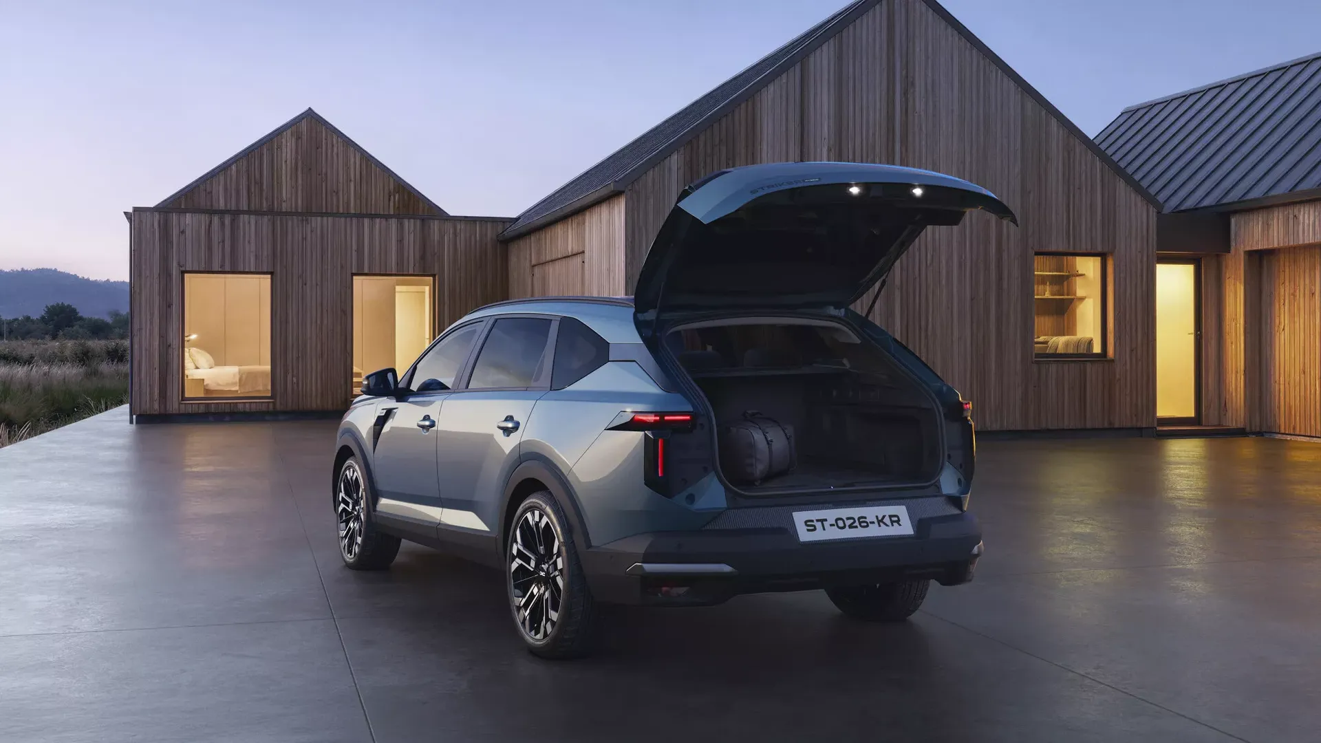 Dacia Striker — tył, otwarty bagażnik z bagażem przy drewnianym domu