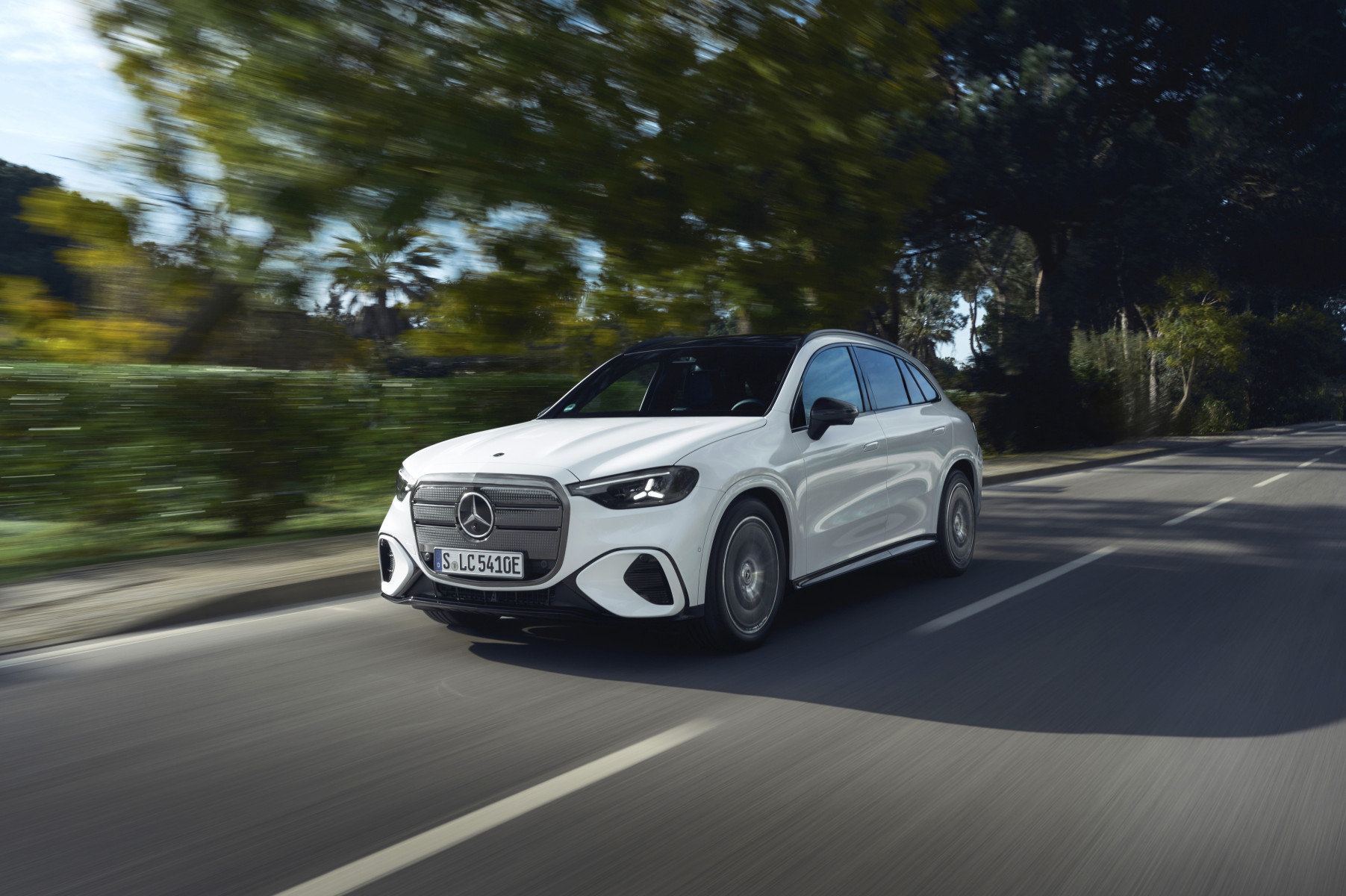 Mercedes-Benz GLC (elektryczny) — przód/bok, dynamiczna jazda drogą wśród drzew