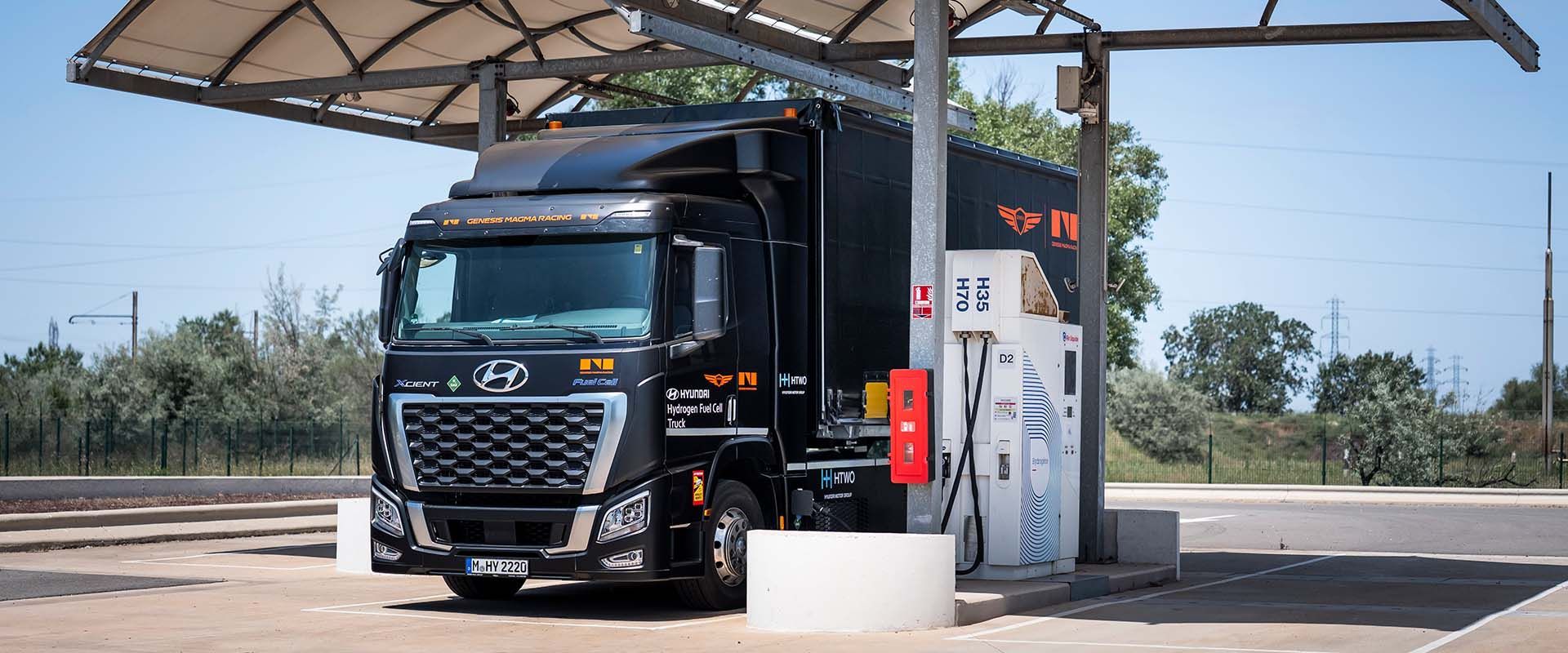 Hyundai Xcient Fuel Cell Genesis Magma Racing — przód, tankowanie wodoru pod zadaszeniem stacji (inne ujęcie)