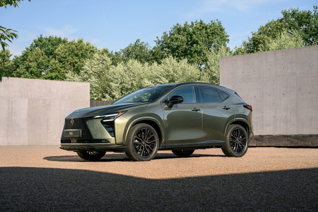 Lexus NX po liftingu — przód 3/4, jazda miejska na tle zieleni i betonowych ścian