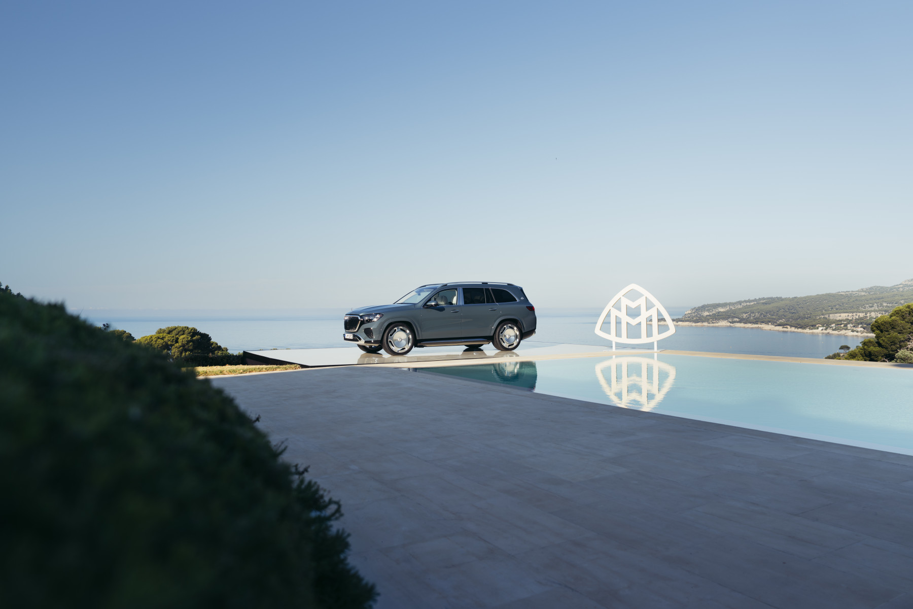 Mercedes-Maybach GLS — widok z boku na tarasie przy basenie, w tle morze; na zdjęciu duże logo Maybach