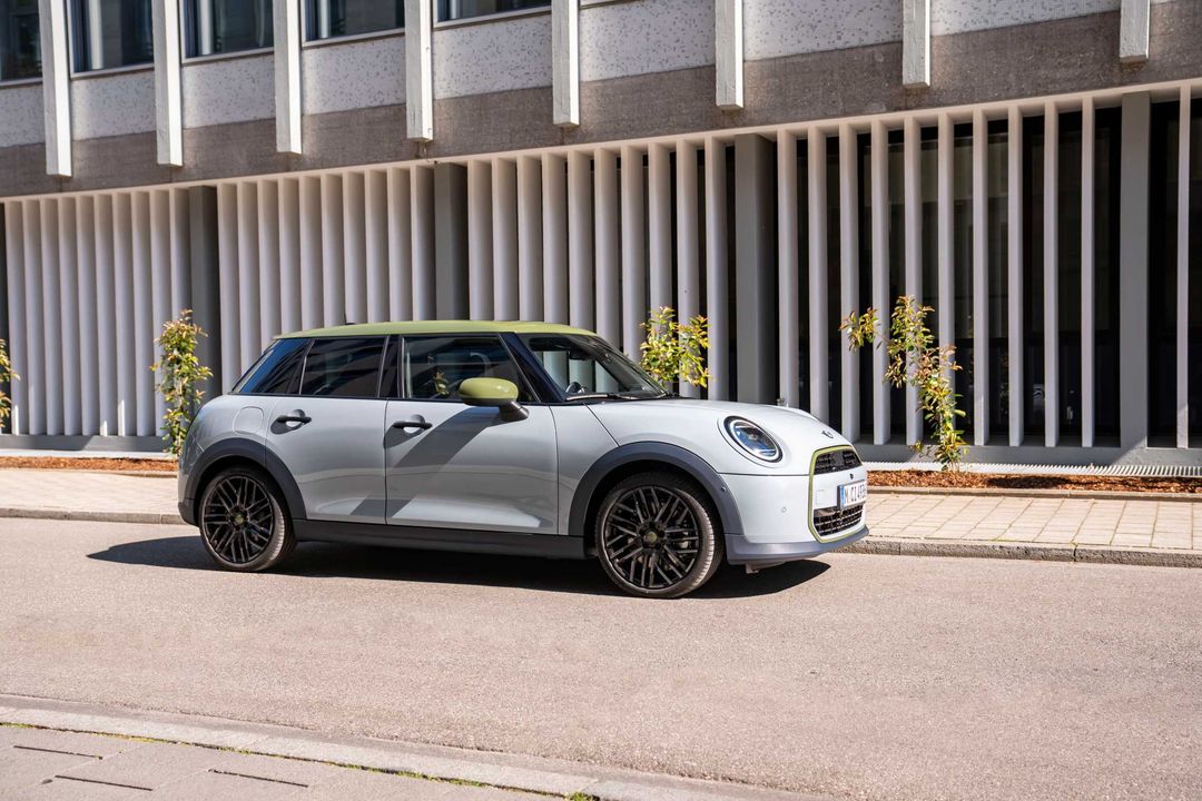 MINI Cooper Paul Smith Edition — bok, srebrne nadwozie z oliwkowym dachem, ujęcie miejskie przy elewacji budynku