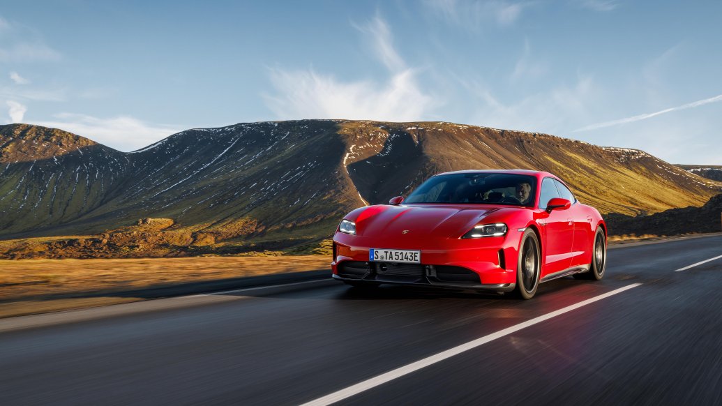 Porsche Taycan w czerwonym kolorze — przód i bok, jazda górską drogą na tle wzgórz