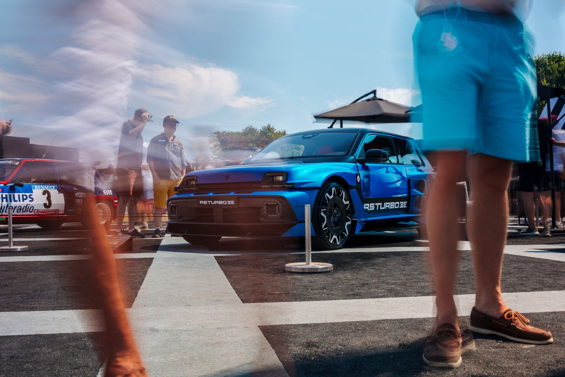 Renault 5 Turbo 3E przesłonięty przez rozmytych, przechodzących zwiedzających na stoisku