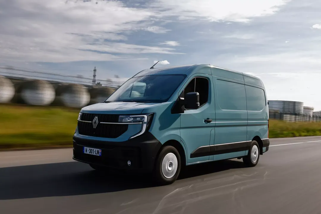 Renault Master (furgon, kolor błękitny) — przód, jazda drogą przy zbiornikach przemysłowych
