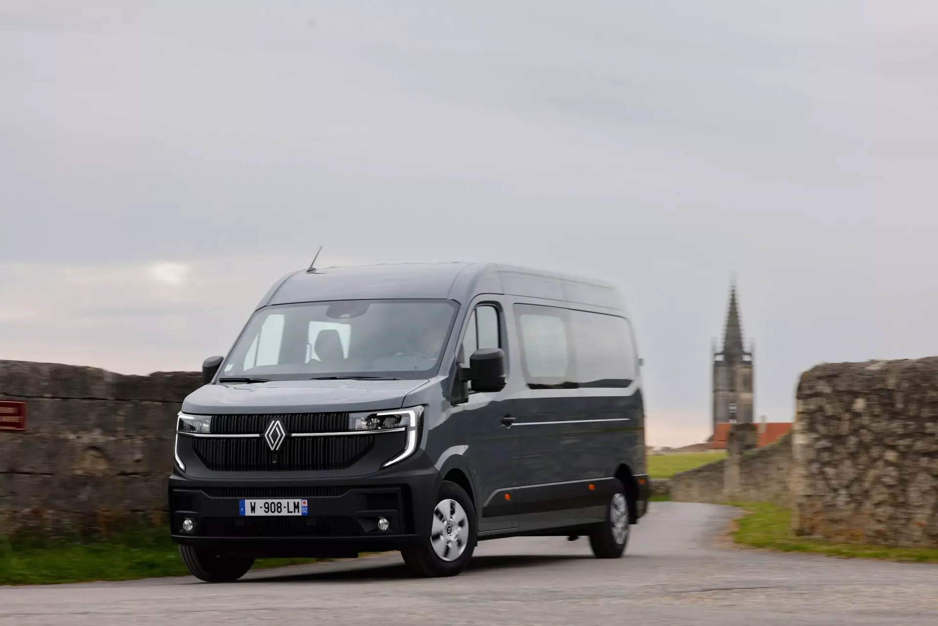 Renault Master (furgon, kolor szary) — przód, postój przy murze z wieżą kościoła w tle