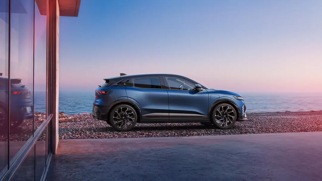 Renault Megane E-Tech Electric — bok, zaparkowany przy nowoczesnym budynku nad plażą