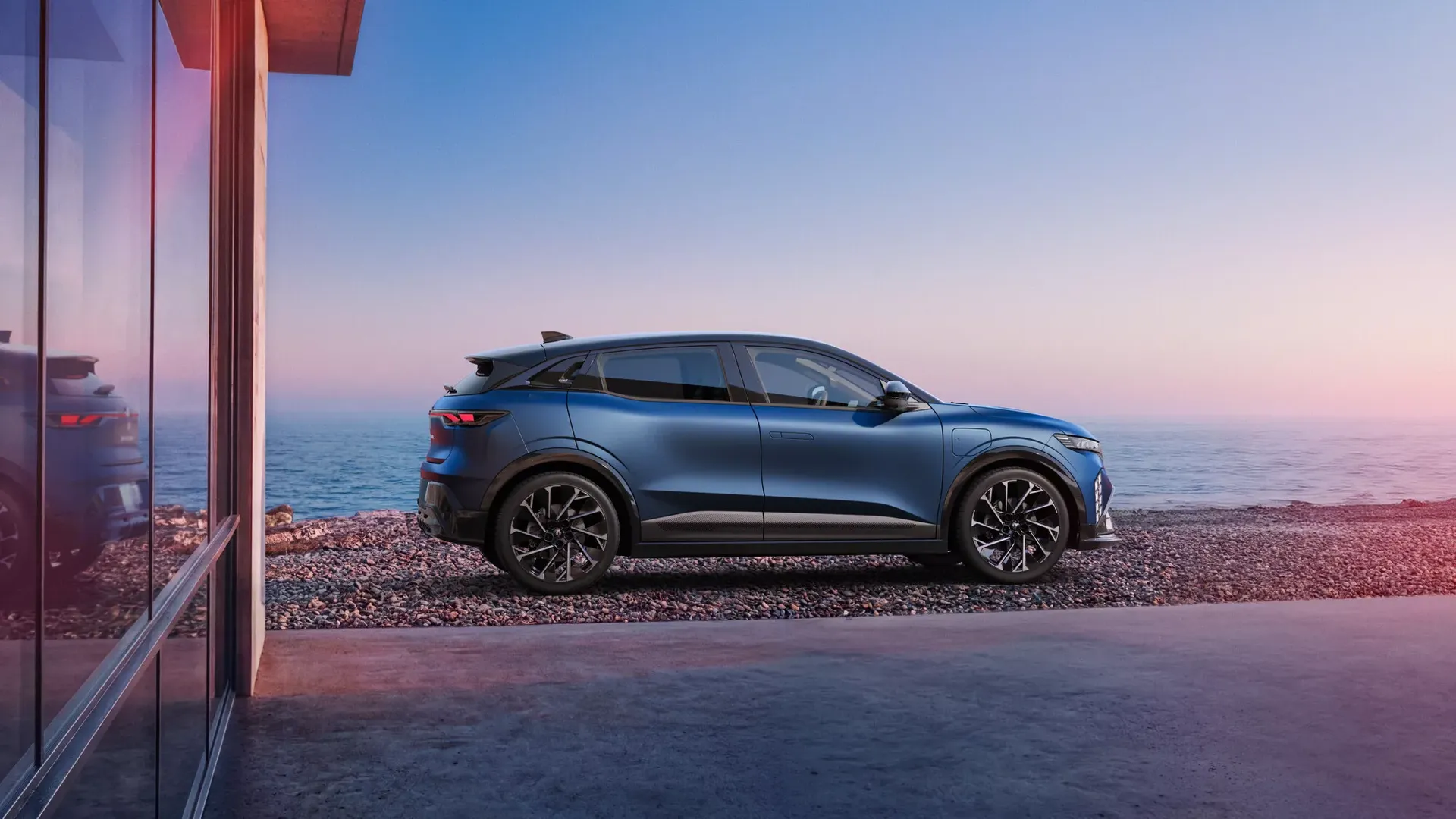 Renault Megane E-Tech Electric — bok, zaparkowany przy nowoczesnym budynku nad plażą