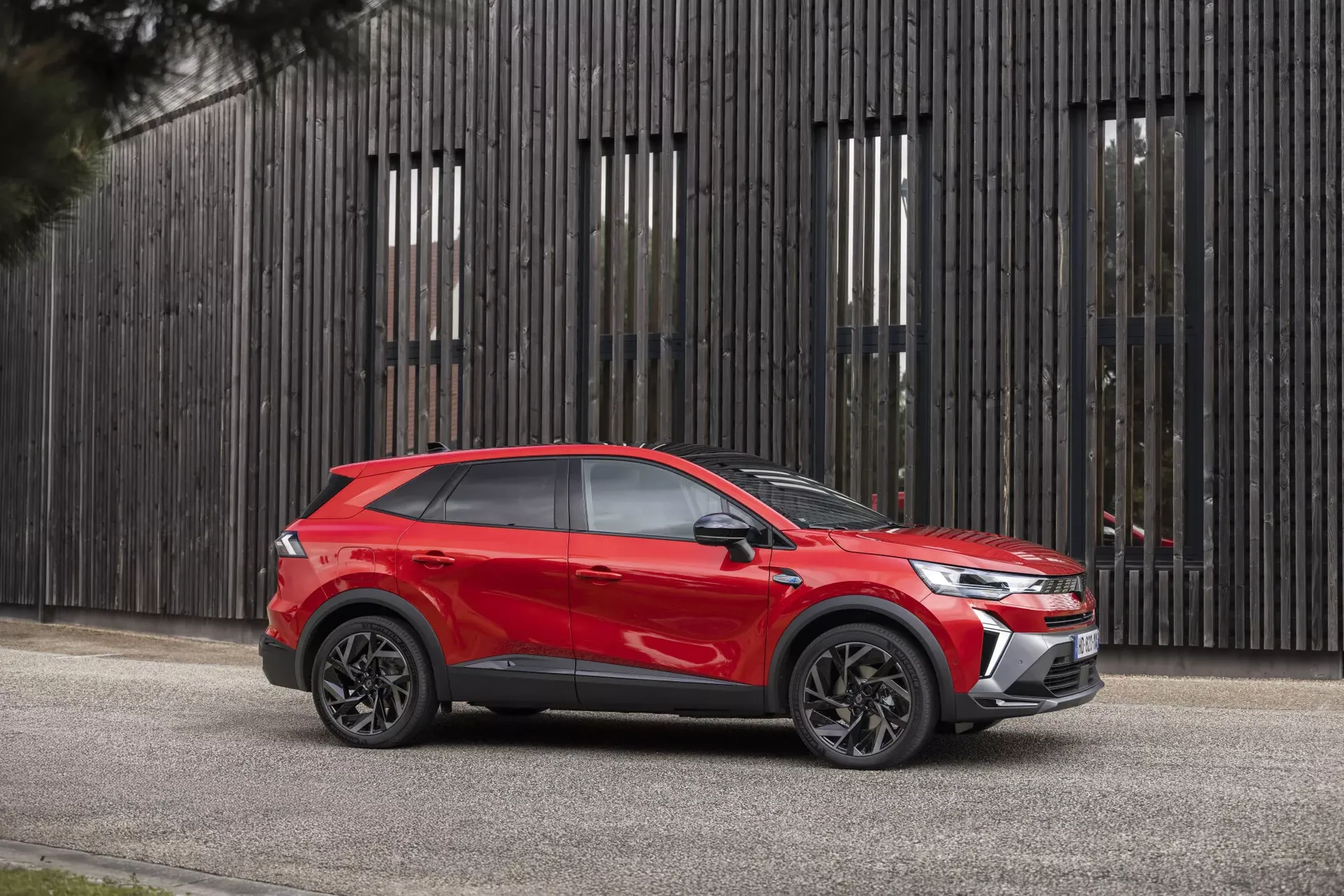 Renault Symbioz — profil boczny, czerwony SUV przy drewnianej ścianie z listew