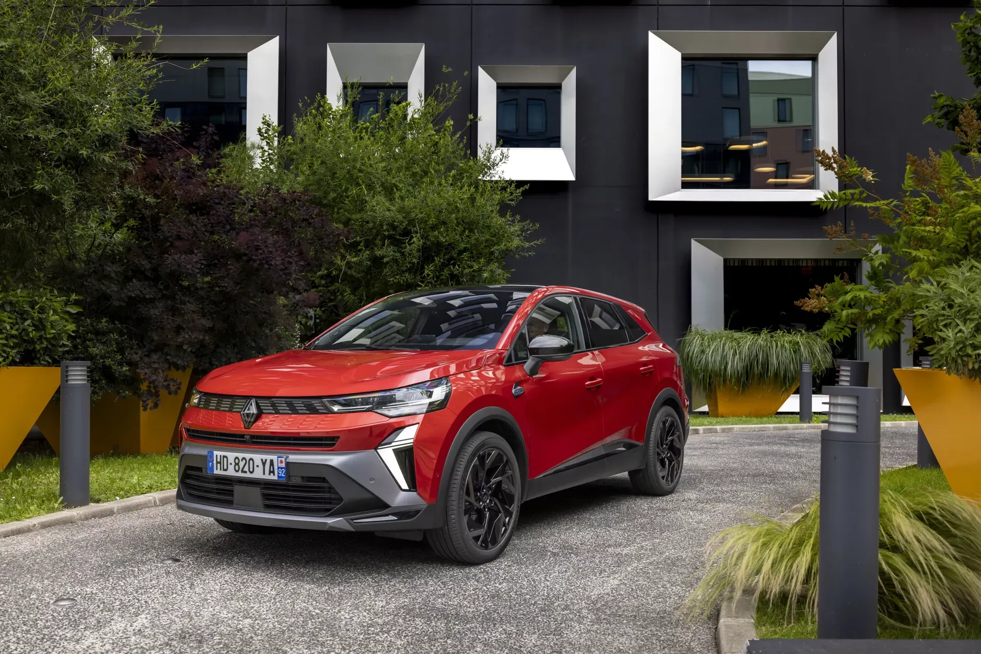 Renault Symbioz — przód 3/4, czerwony SUV na dziedzińcu nowoczesnego budynku