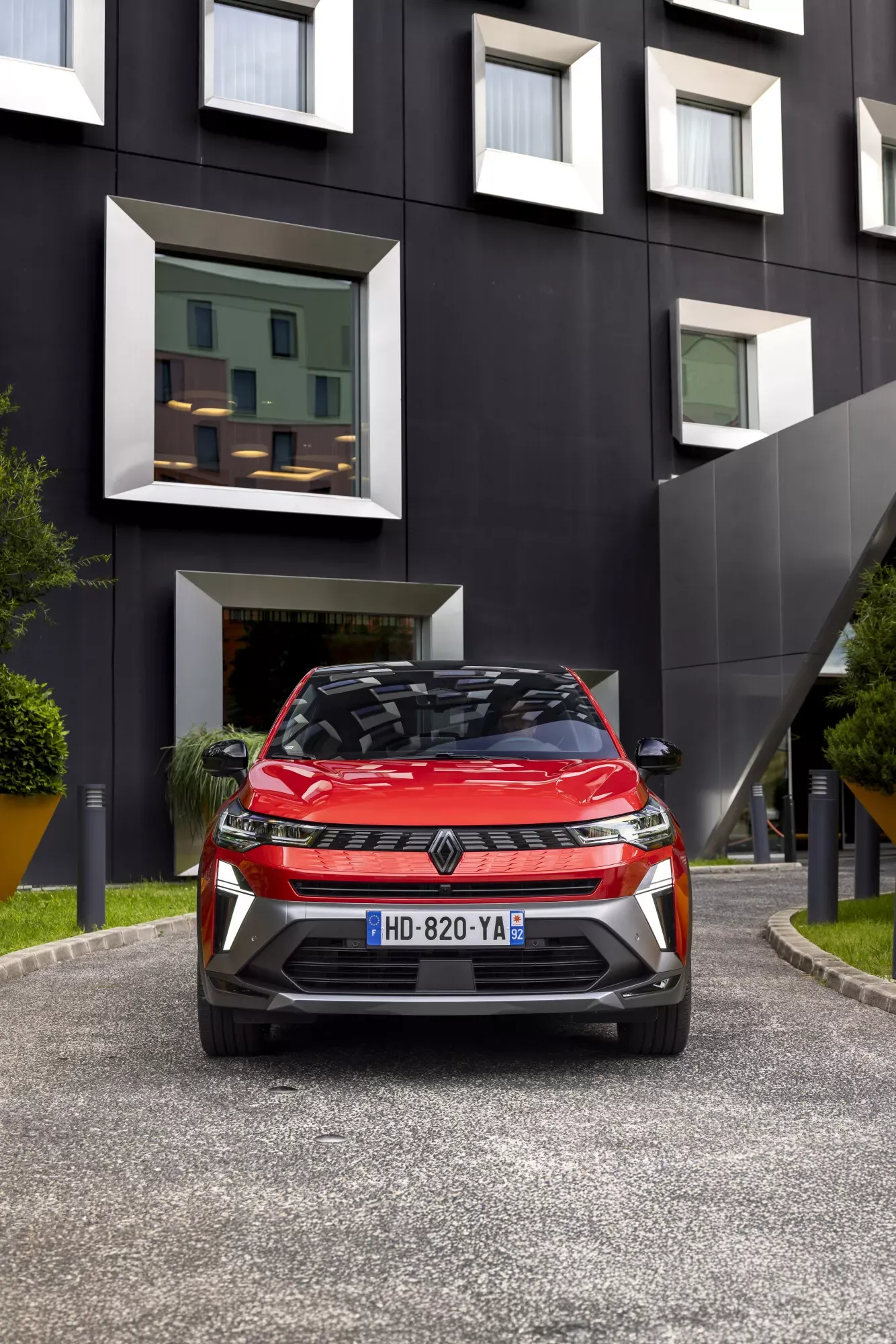 Renault Symbioz — przód, czerwony SUV na dziedzińcu, w tle elewacja budynku