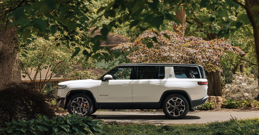 Rivian R2 — bok, biały SUV w otoczeniu zieleni podmiejskiej, ujęcie profilowe
