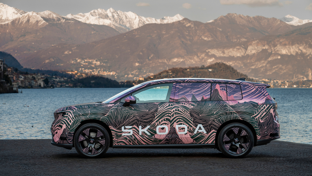 Škoda Peaq — prototyp w graficznym kamuflażu, widok boczny przy alpejskim jeziorze z ośnieżonymi szczytami w tle
