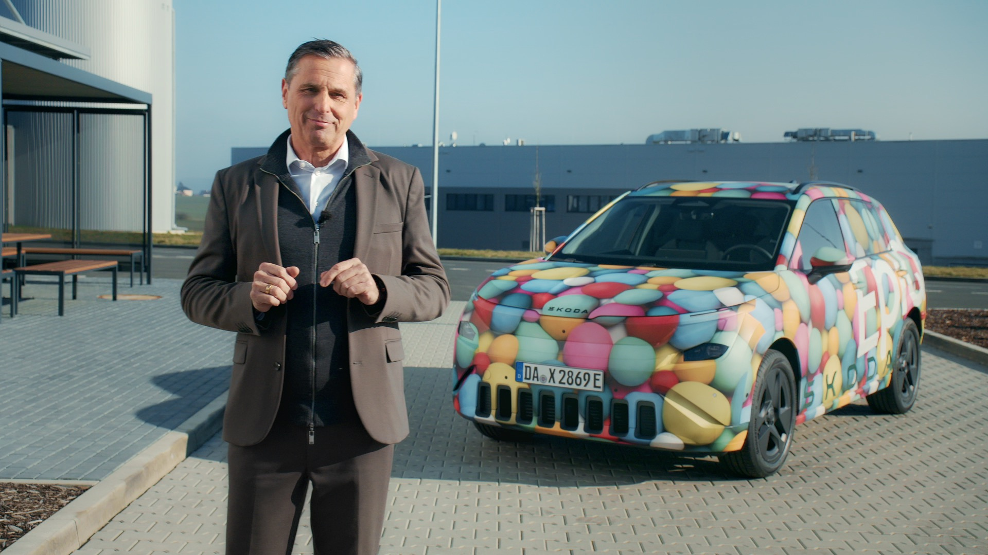 Škoda Peaq — menedżer marki stojący przed prototypem w kolorowym kamuflażu na terenie fabryki, zdjęcie PR z osobą na pierwszym planie